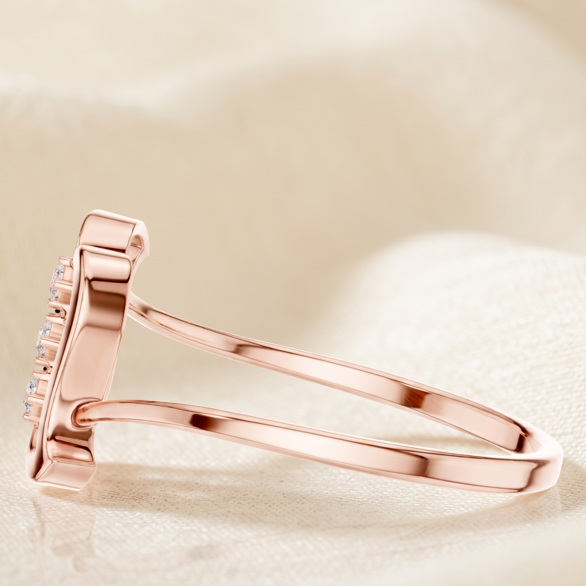 A rose gold ring with a rectangular pavé setting, photographed on a soft, textured cream fabric background.