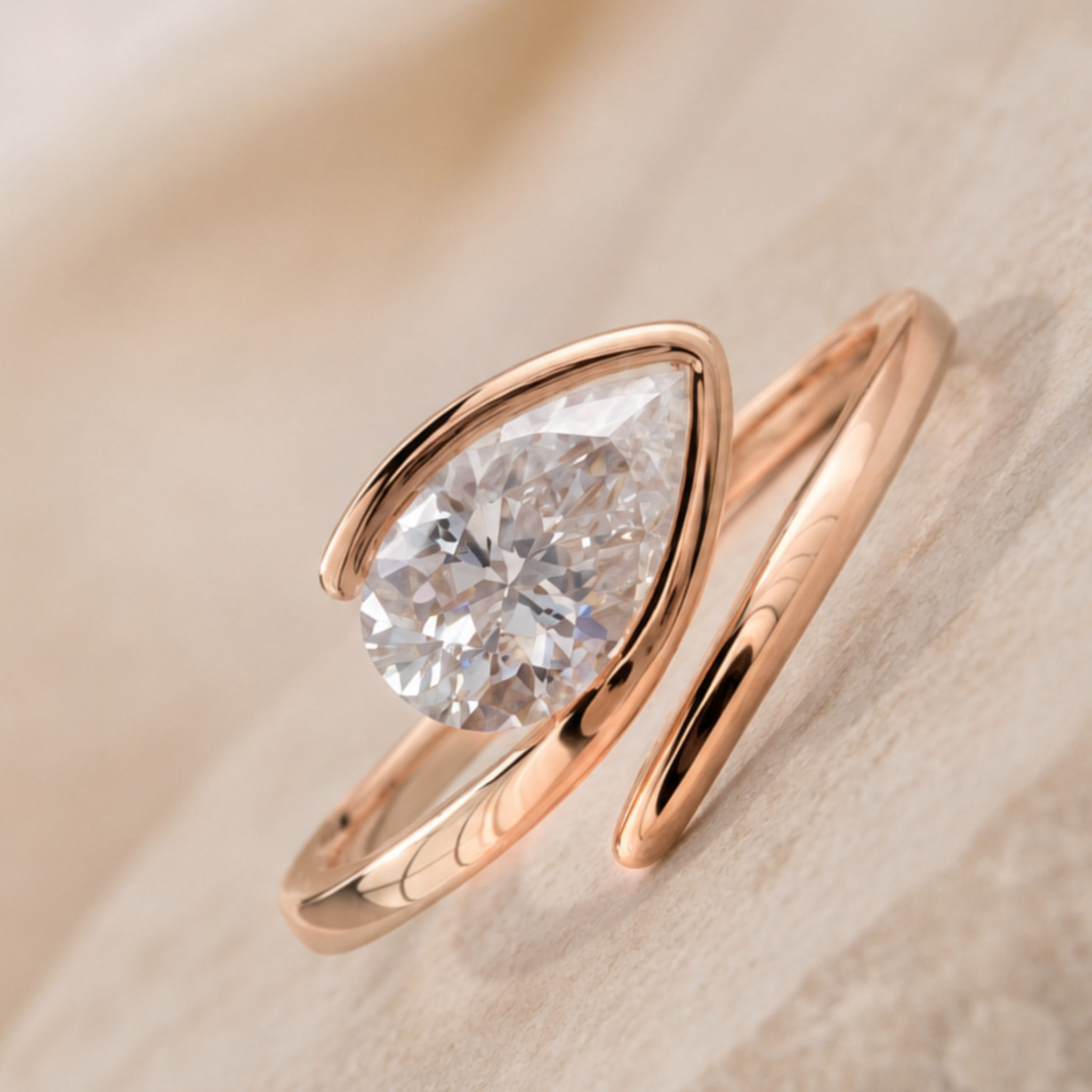 A rose gold ring featuring a large pear-cut clear gemstone in a curved setting, resting on a soft beige textured surface.