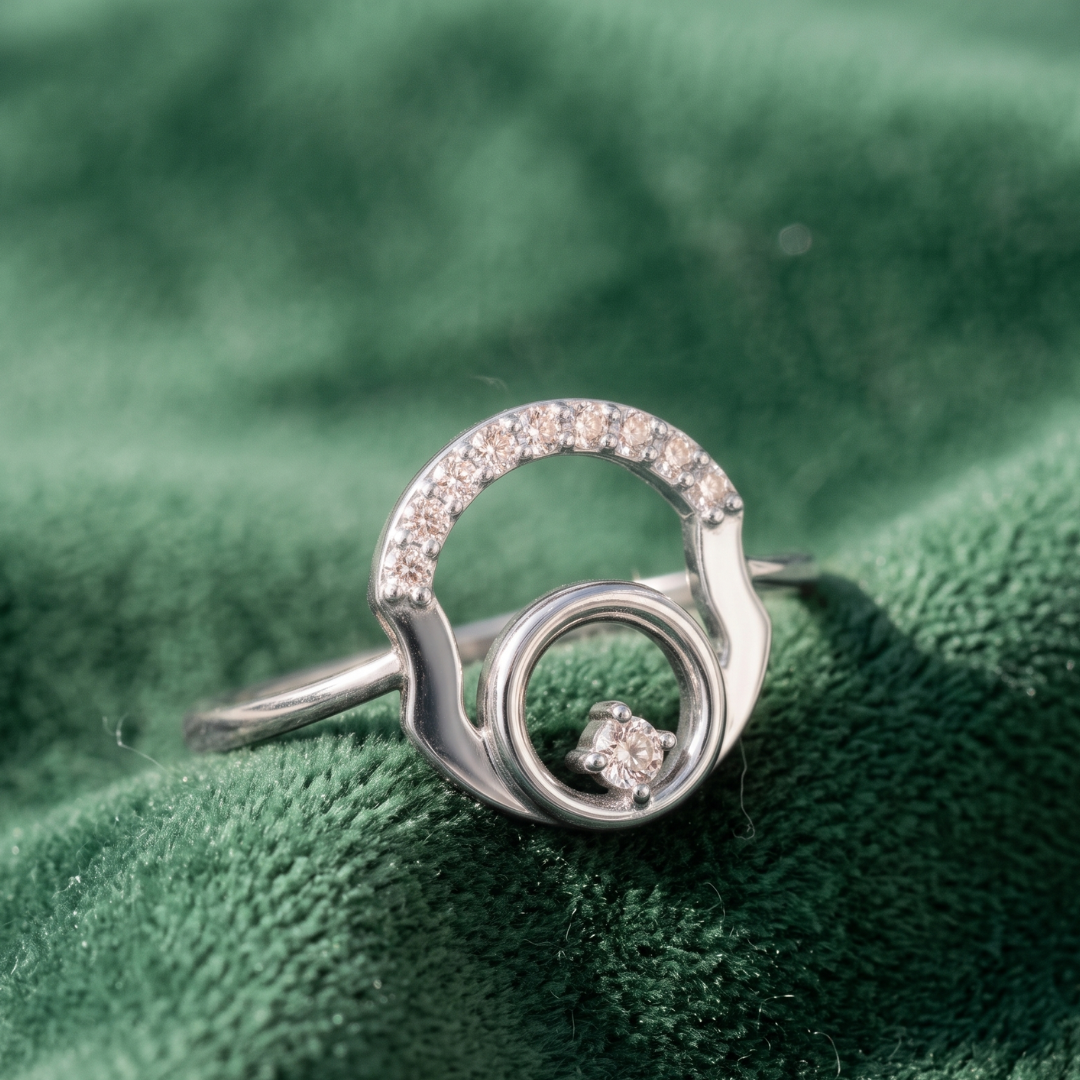 A silver-toned ring with a crescent-shaped top set with small clear stones and a central circular detail, displayed on a textured green velvet surface.