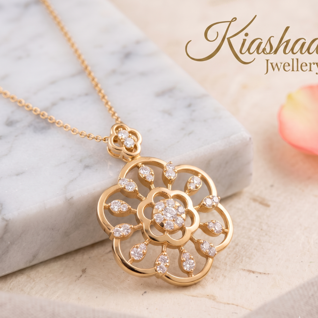 A gold floral pendant necklace with clear stones, displayed on a white marble block with a soft pink rose petal in the background. The brand name 'Kiashaa Jewellery' is visible in the top right corner.