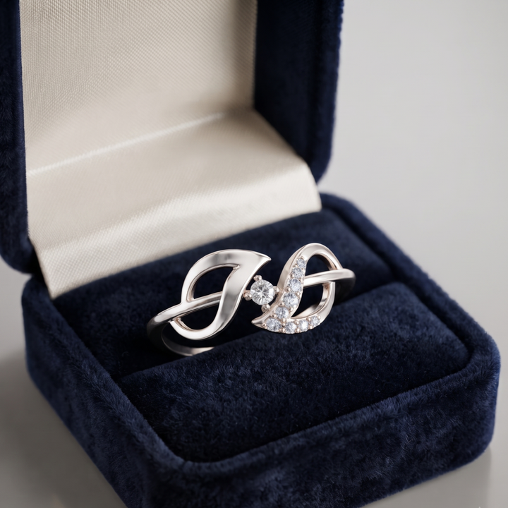 A silver ring with a heart-shaped pavé setting and a central clear gemstone, displayed inside an open dark blue velvet ring box with a cream satin lining.