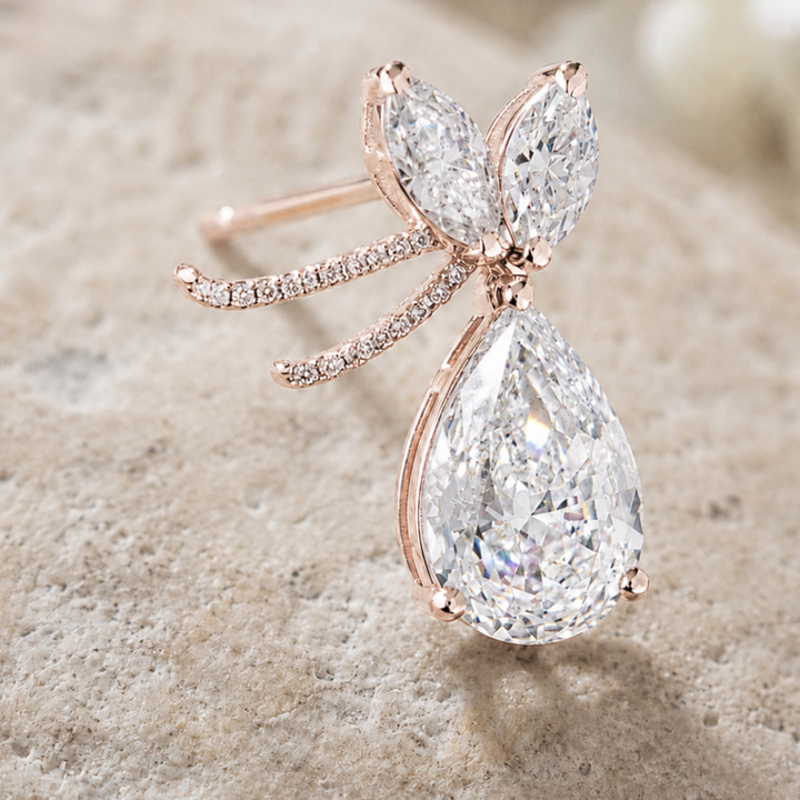 Rose gold butterfly ring with pear-cut and marquise-cut clear gemstones, displayed on a textured beige stone surface.
