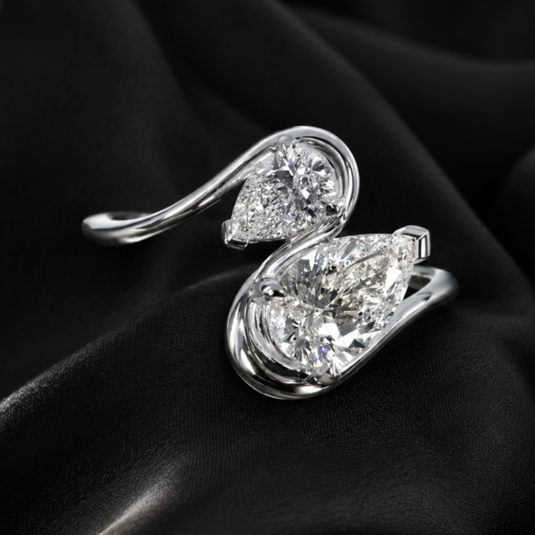 A silver-toned ring featuring two large pear-cut clear gemstones in a swirling open-band design, photographed on draped black fabric.