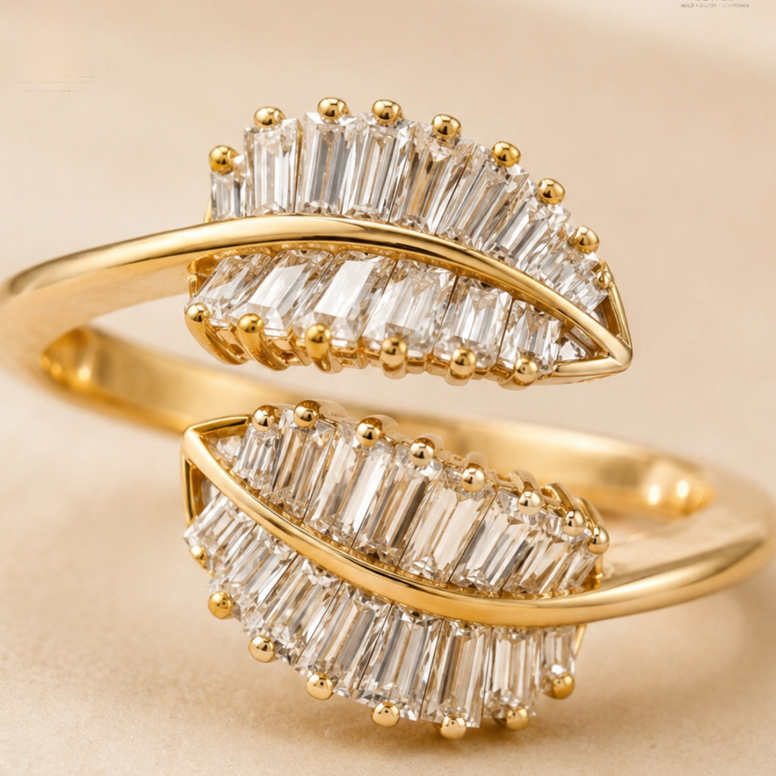 A close-up of a gold ring featuring two leaf-shaped settings adorned with clear baguette and round-cut stones, set against a soft beige background.