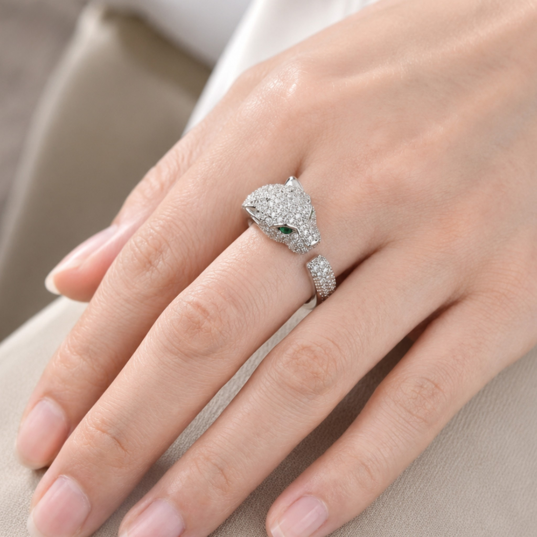 A close-up of a hand wearing a silver-toned snake ring with pavé-set clear stones and a small green eye accent, resting on a neutral beige surface.