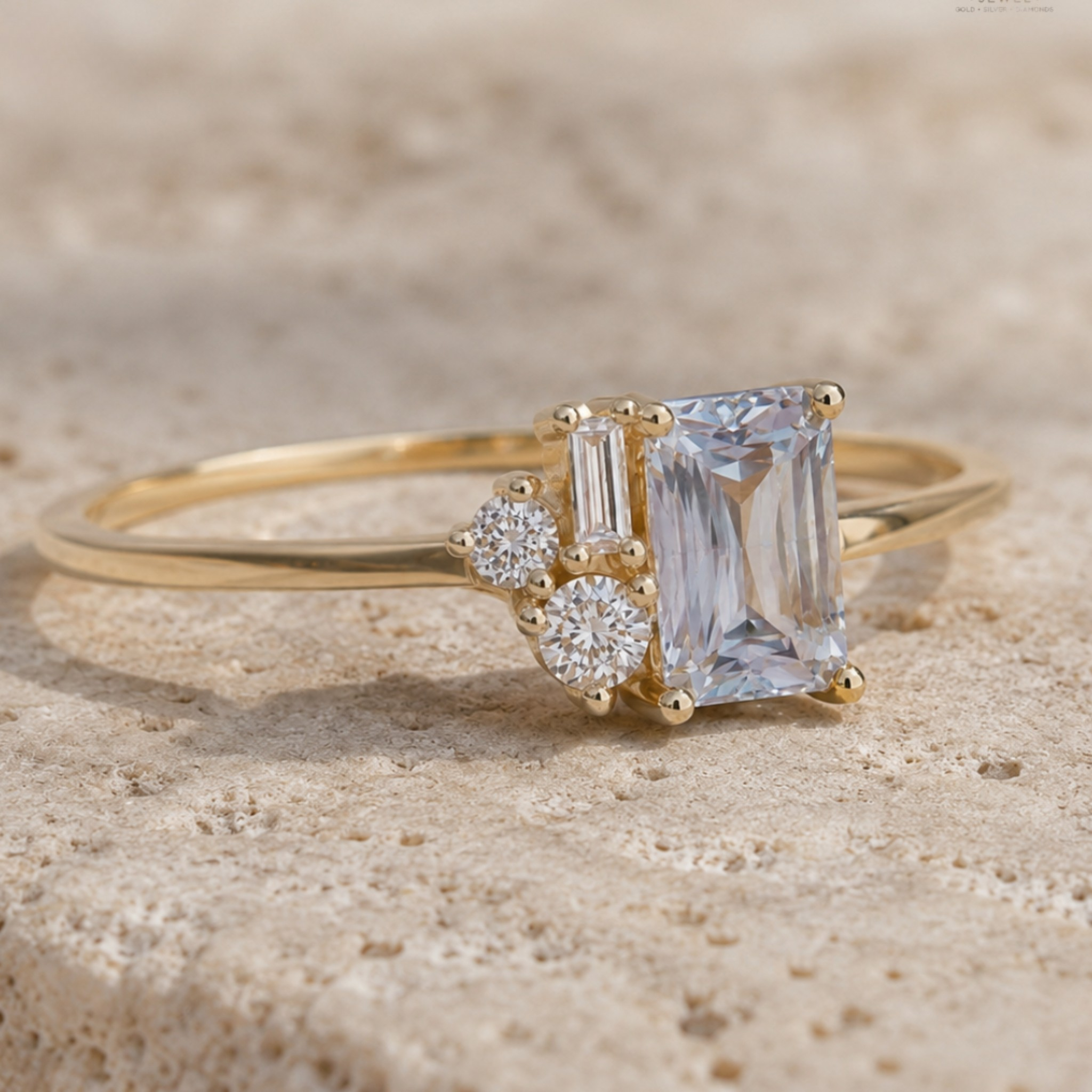 A yellow gold ring featuring a large emerald-cut clear center stone and two smaller clear accent stones, photographed on a textured beige stone surface.