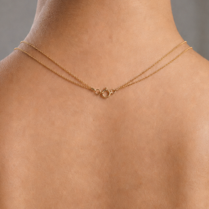 A delicate gold double-strand necklace with a small central ring detail, shown worn on a model's neck.