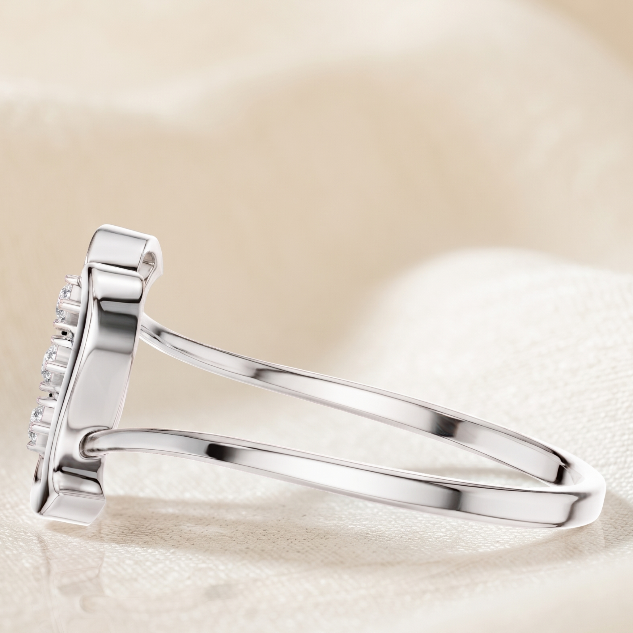 A silver ring with a rectangular pavé diamond setting, shown in a close-up studio shot on a soft beige fabric background.