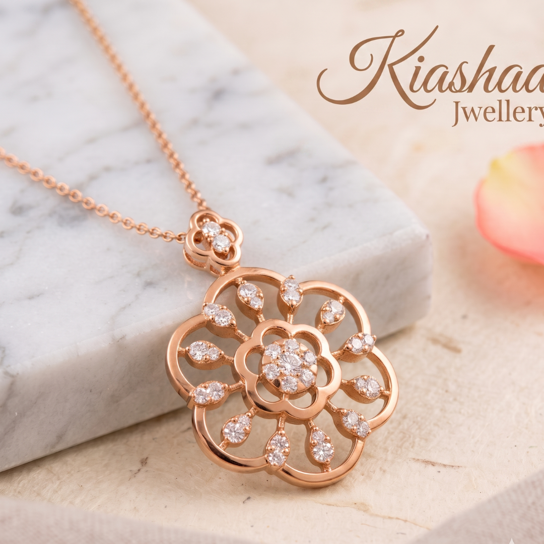 Rose gold floral pendant necklace with clear stones, displayed on a white marble block with a soft pink flower petal in the background. The brand name 'Kiashaa Jewellery' is visible in the top right corner.