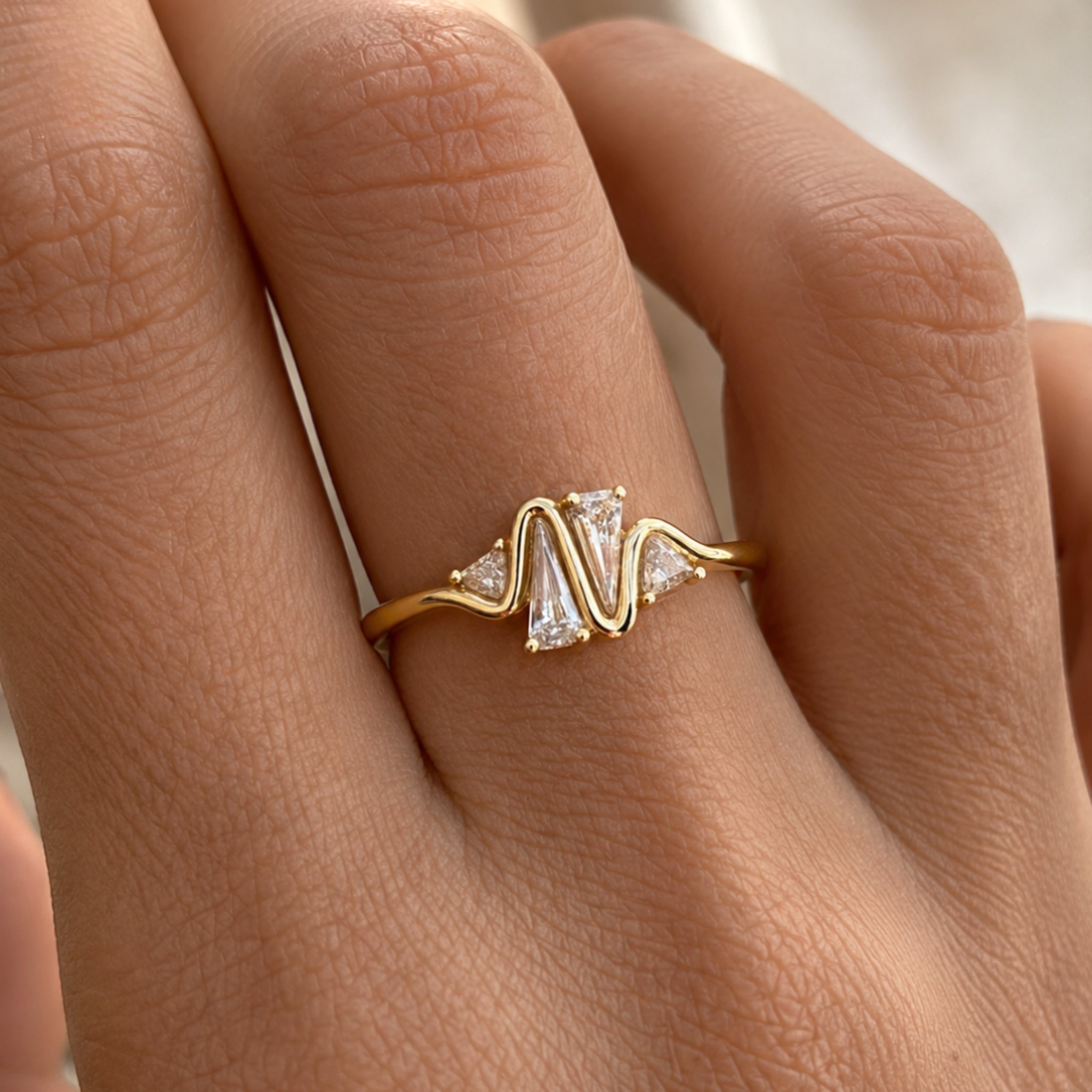 A gold ring with a wavy, zigzag design and clear rectangular gemstones, shown worn on a person's finger.