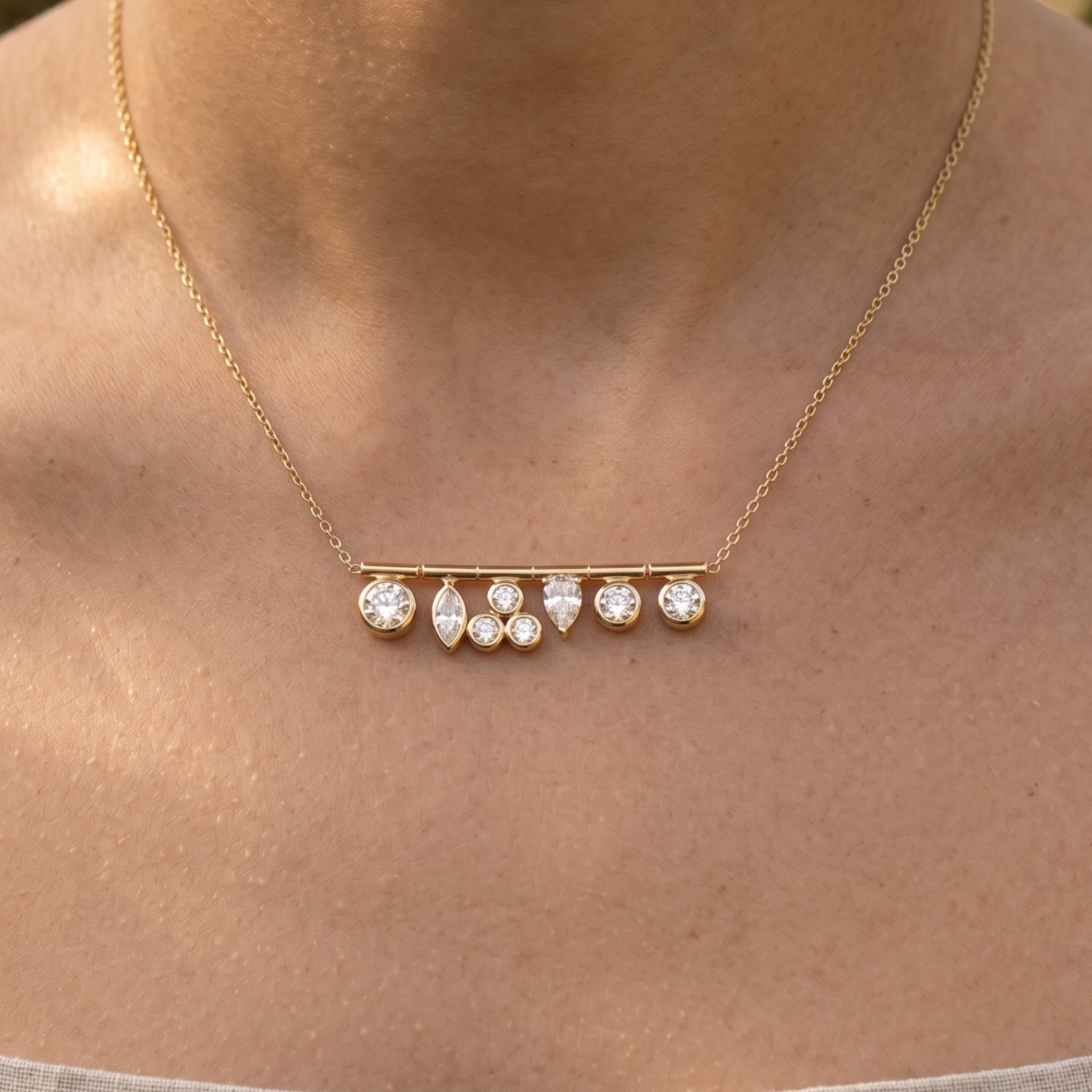 A delicate gold chain necklace with a horizontal bar pendant featuring small clear gemstones, shown worn on a person's neck.
