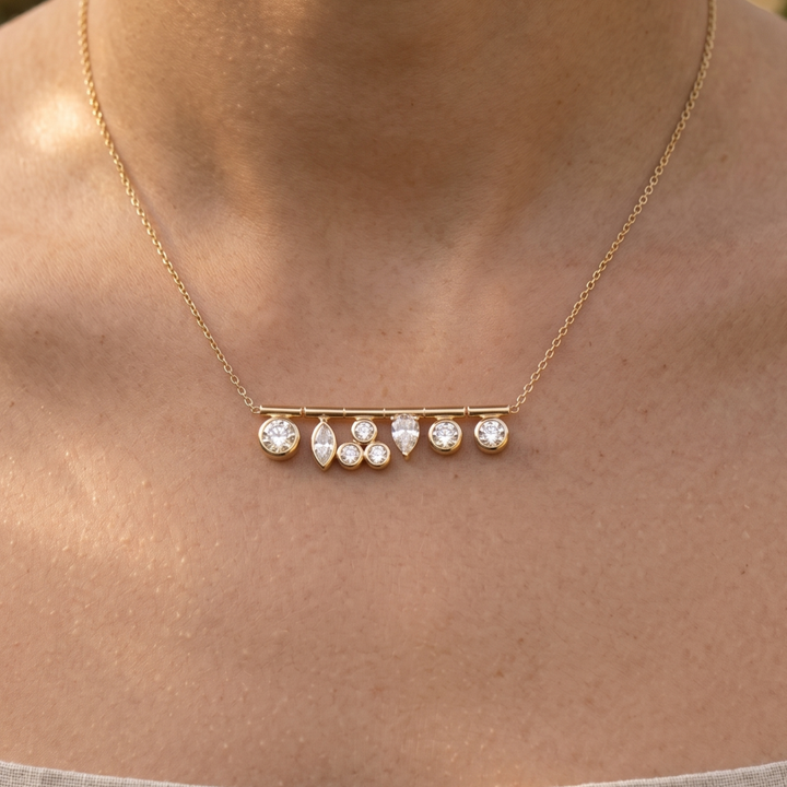 A delicate gold chain necklace with a horizontal bar pendant featuring small clear gemstones, shown worn on a person's neck.
