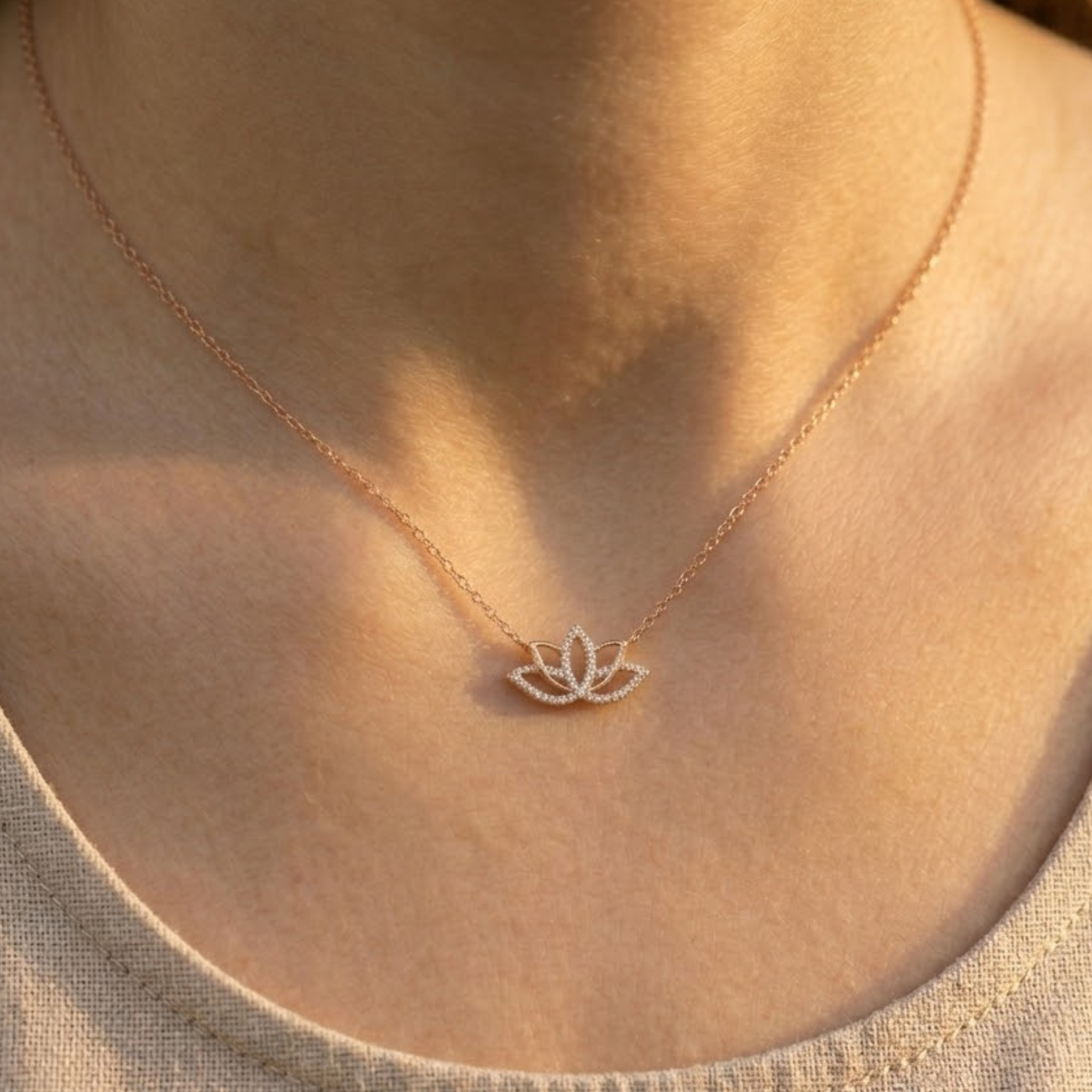 A close-up of a person's neck and chest wearing a delicate rose gold necklace with a small lotus flower pendant.