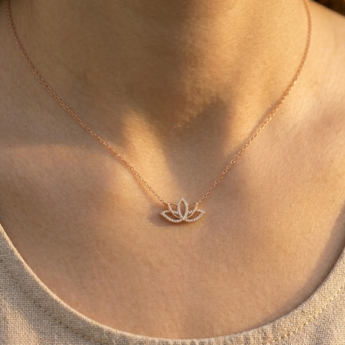 A close-up of a person's neck and chest wearing a delicate rose gold necklace with a small lotus flower pendant.
