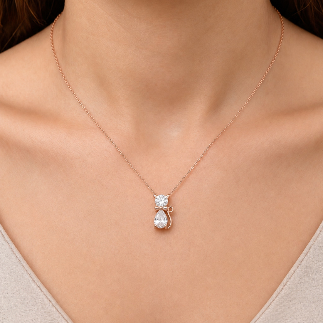 A close-up of a person's neck and chest wearing a delicate rose gold necklace with a pendant shaped like a small cat holding a pear-shaped clear gemstone.