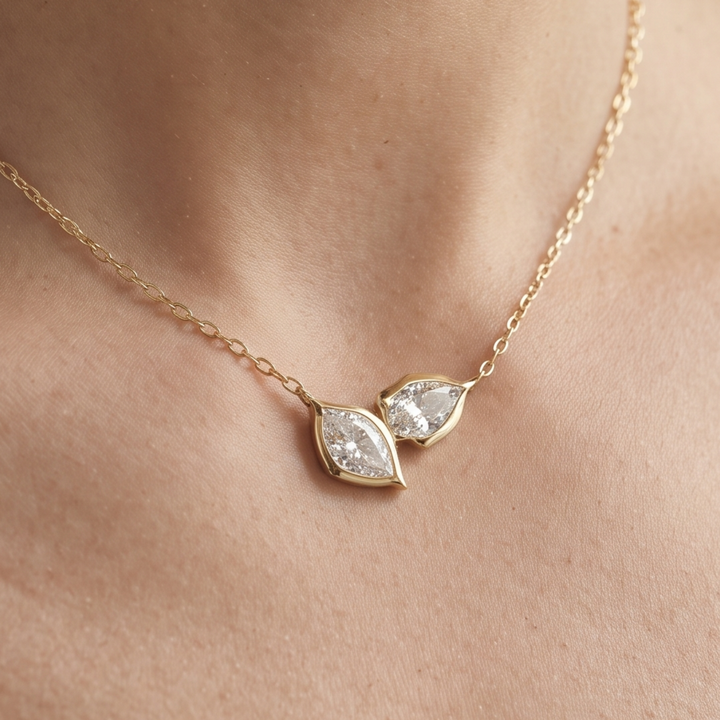 A delicate gold chain necklace with two marquise-shaped clear gemstones in gold settings, worn on a person's neck.