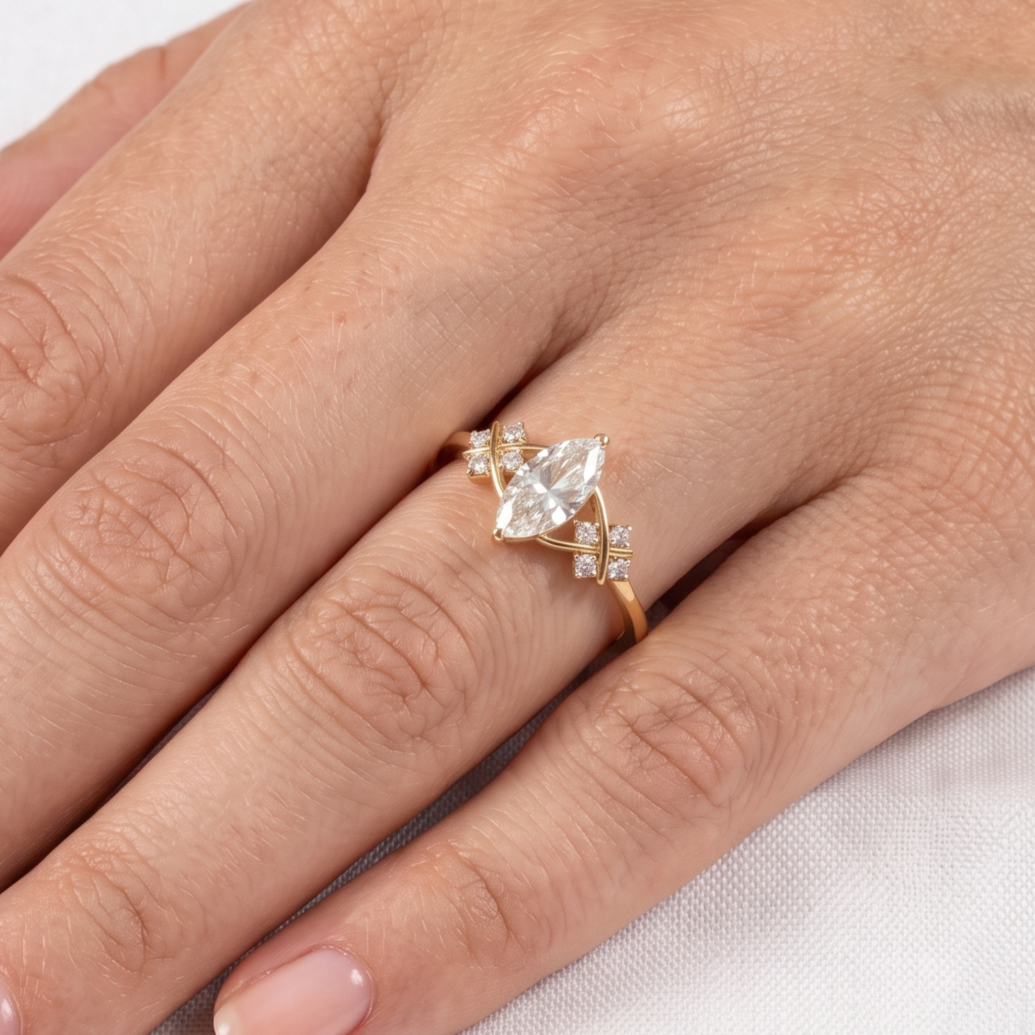 A gold ring with a marquise-cut clear center stone and small accent stones, shown worn on a person's finger against a light fabric background.