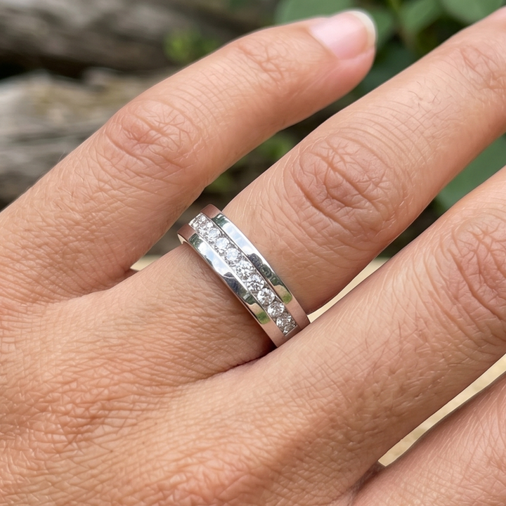 A silver band ring with a channel-set row of small clear stones, shown worn on a person's finger against a blurred outdoor background.
