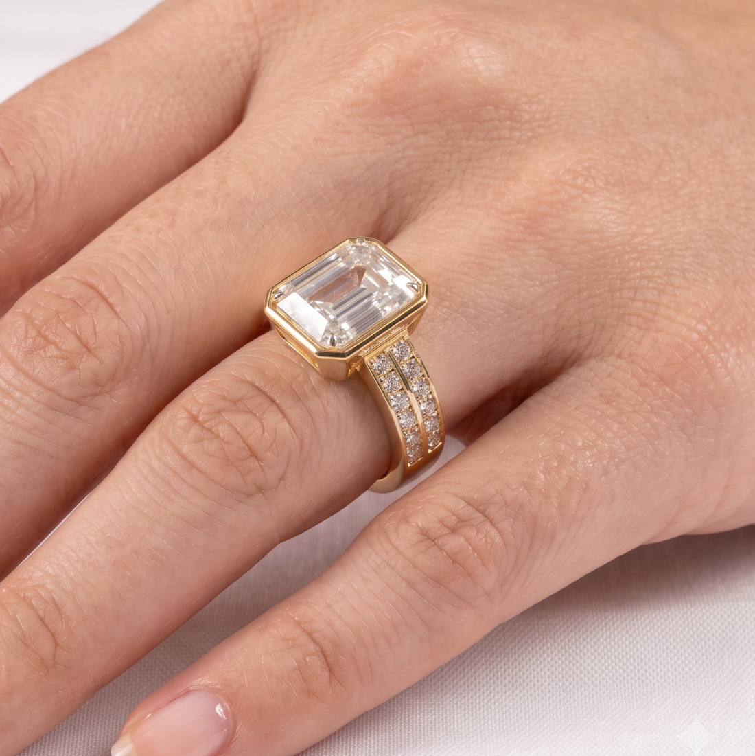 A close-up of a hand wearing a yellow gold ring with a large rectangular emerald-cut clear center stone and a double-row channel-set diamond band.