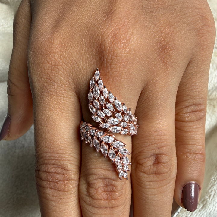 A close-up of a hand wearing a rose gold ring with marquise-cut clear stones arranged in a layered, wing-like pattern.