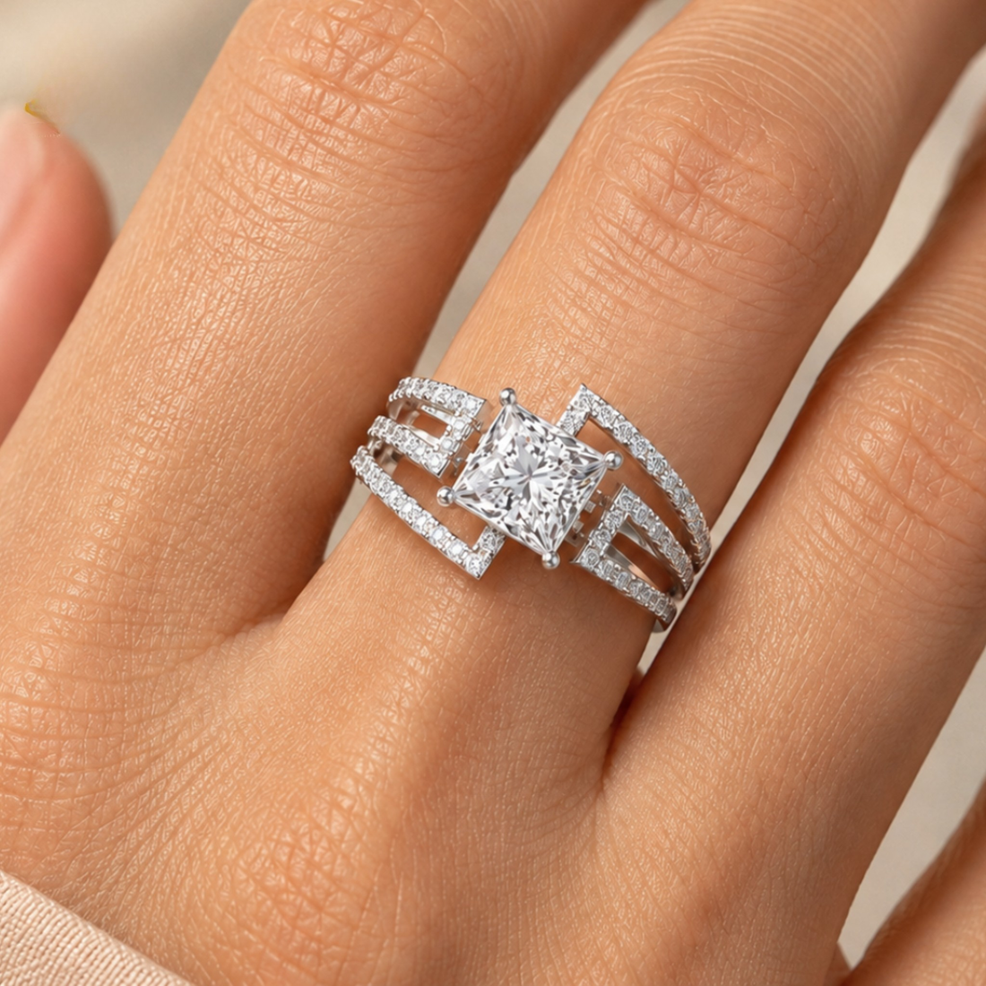A close-up of a hand wearing a silver-toned ring with a large princess-cut center stone and smaller surrounding stones in an open pavé-style band design.