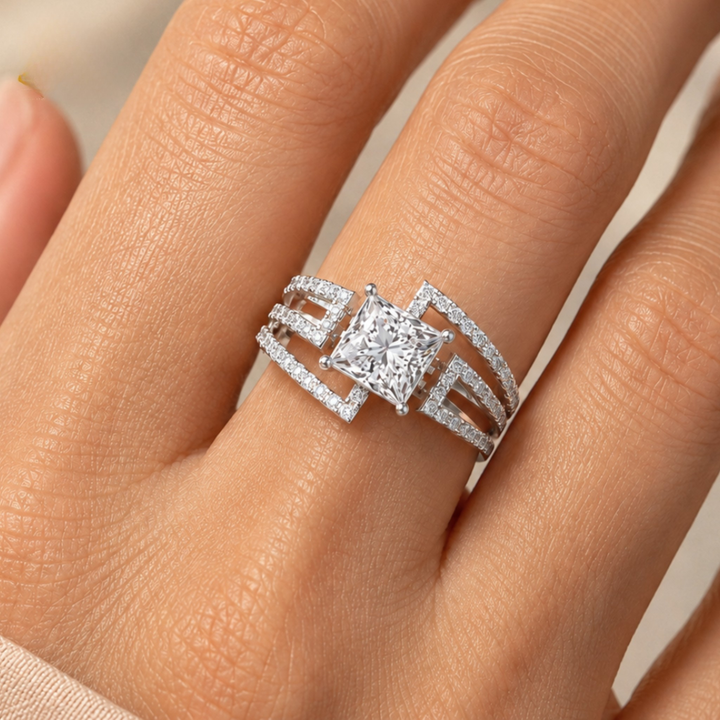 A close-up of a hand wearing a silver-toned ring with a large princess-cut center stone and smaller surrounding stones in an open pavé-style band design.