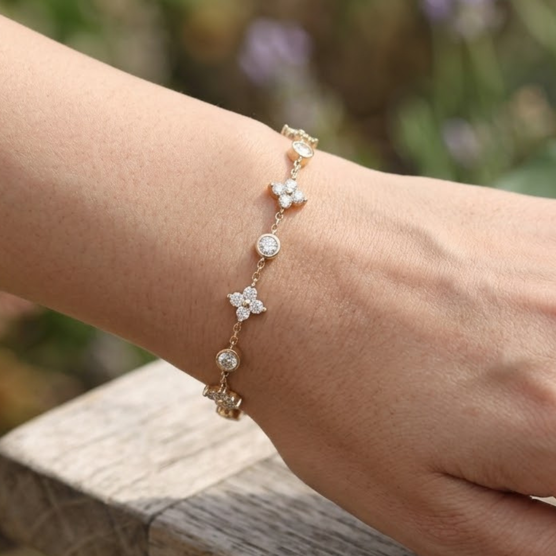 Floral round diamond station bracelet worn on the wrist in polished yellow gold.