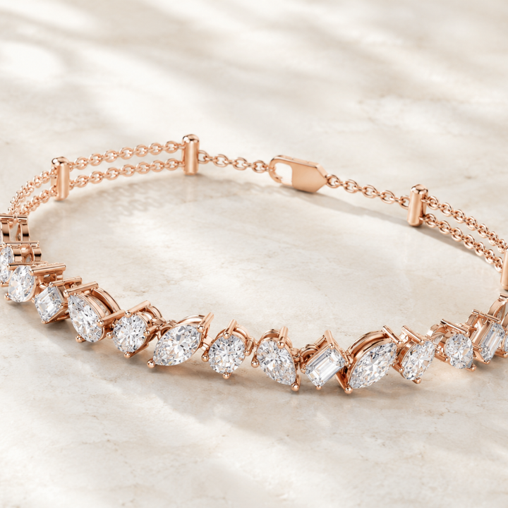 Rose gold tennis bracelet with marquise and baguette-cut clear stones, displayed on a light marble surface.