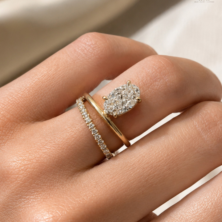 A close-up of a hand wearing two gold rings with diamonds. The primary ring features a large pear-cut diamond cluster, while the secondary ring is a thin diamond-studded band.