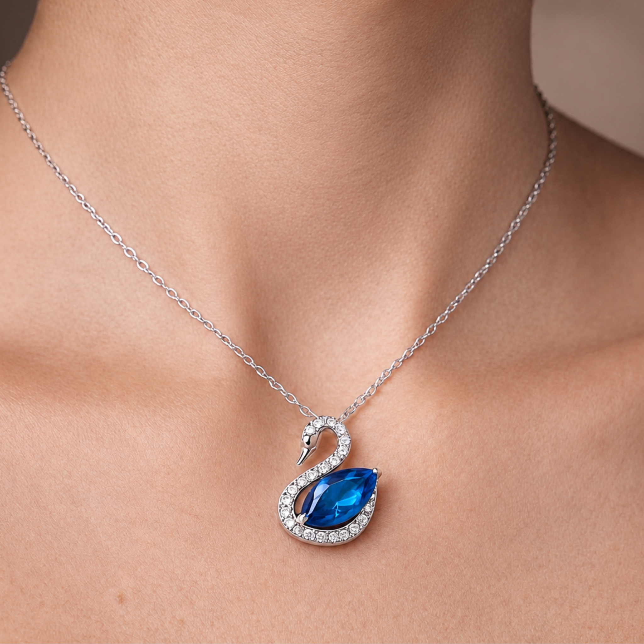 A close-up of a silver-toned swan necklace with a blue marquise-cut center stone and small clear stones, worn on a model's neck.