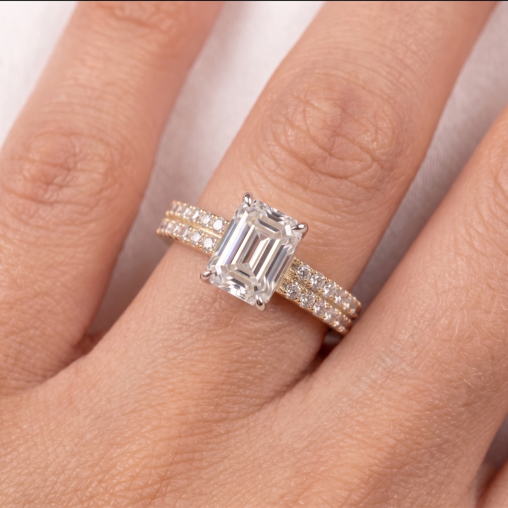 An emerald-cut diamond engagement ring with a silver-colored band accented by small pavé diamonds, shown worn on a hand.