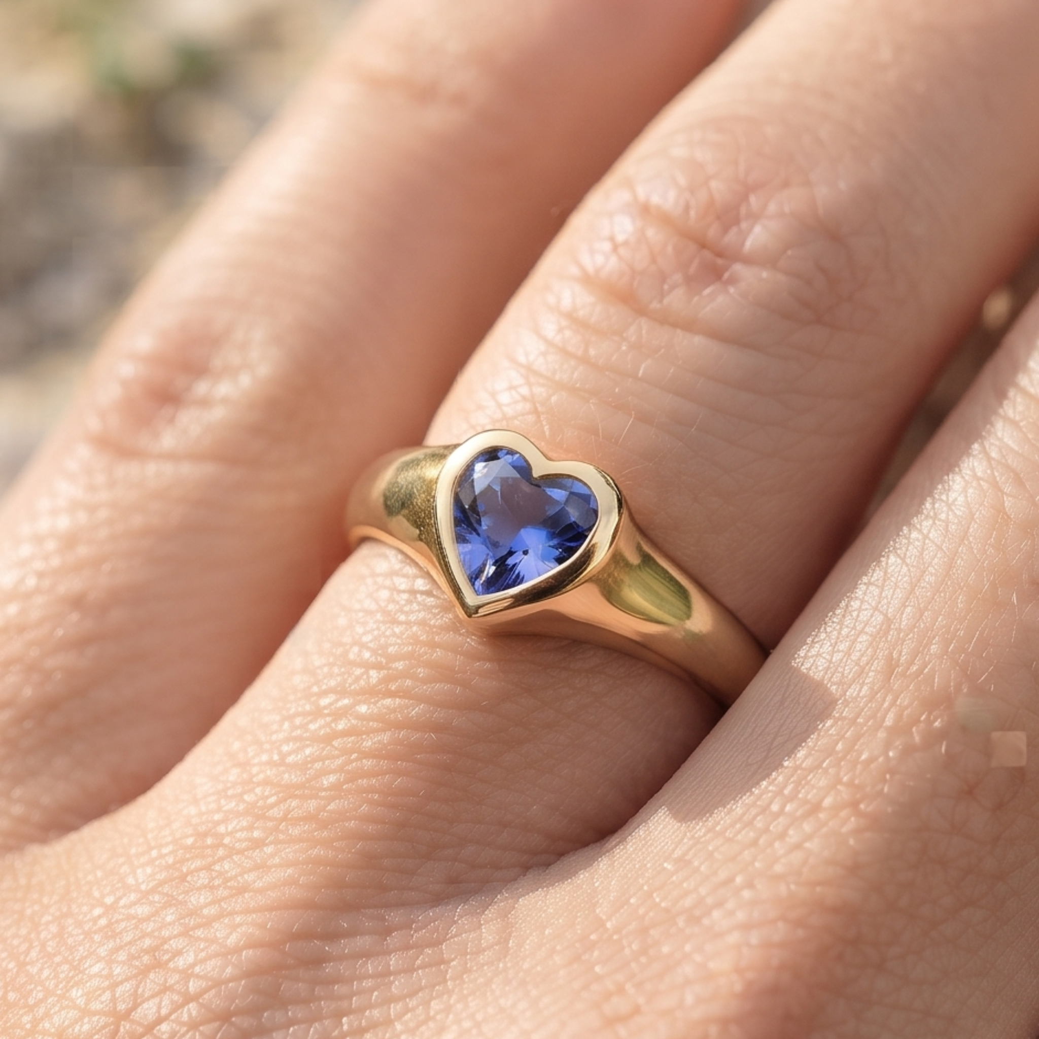 A gold heart-shaped ring with a blue gemstone, worn on a person's finger.
