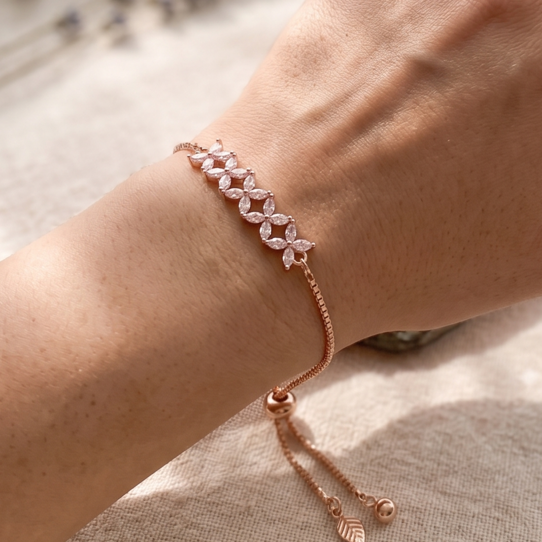 A delicate rose gold bracelet with marquise-cut clear stones arranged in a leaf pattern, shown worn on a person's wrist against a soft neutral background.