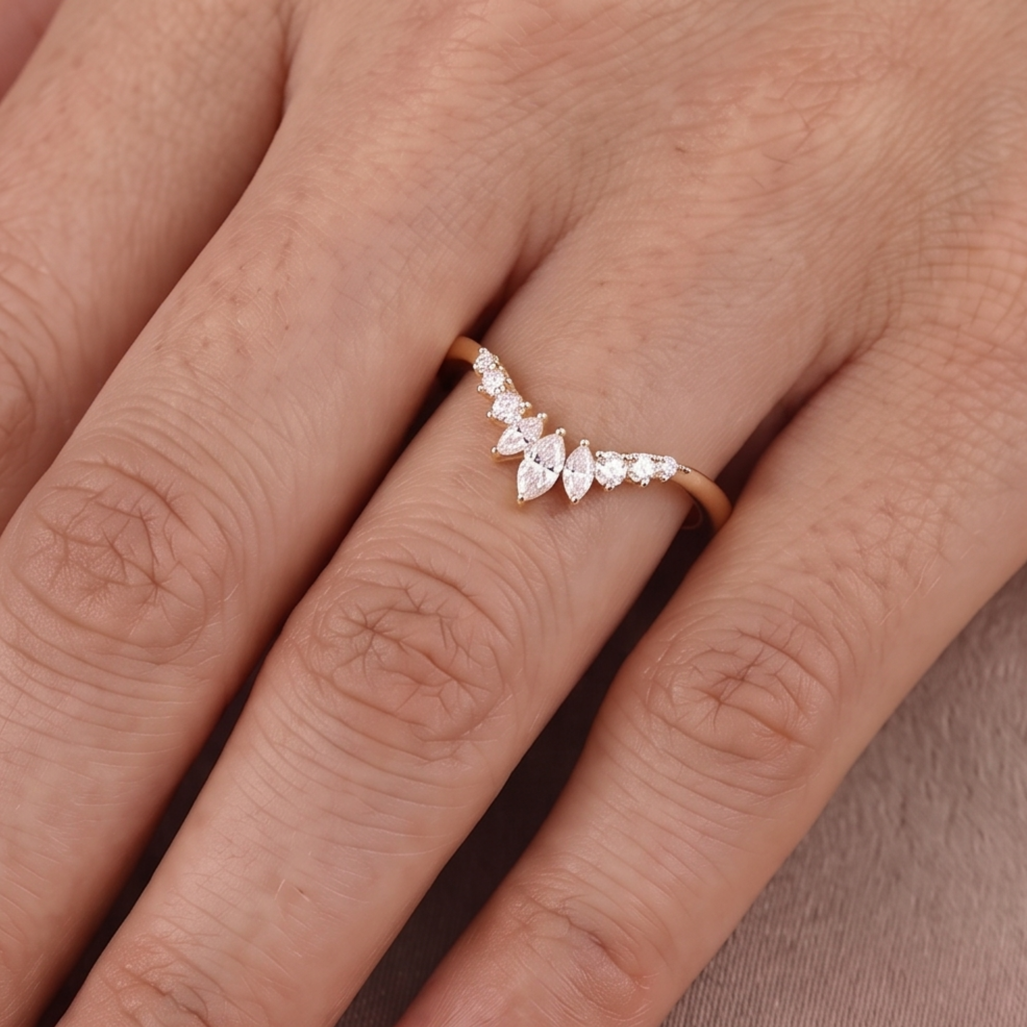 A close-up of a hand wearing a delicate rose gold ring with a curved row of clear marquise-cut and round-cut gemstones.
