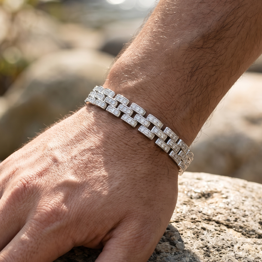 A close-up of a silver-toned link bracelet with pavé-set clear stones worn on a person's wrist, resting against a rock outdoors.