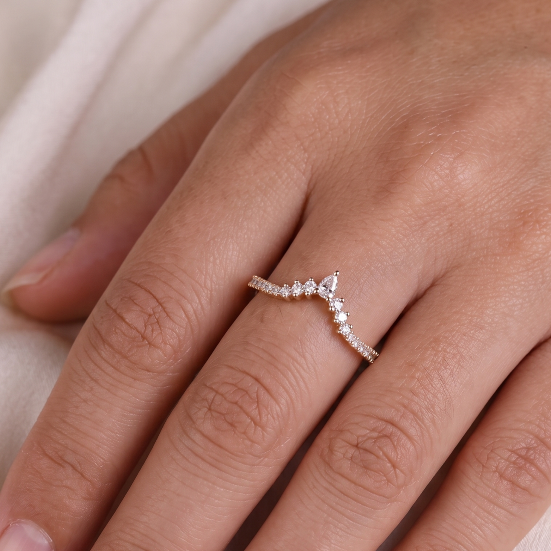 A delicate silver ring with a wavy, pavé-set band and a small triangular cluster of clear stones at the center, shown worn on a finger.