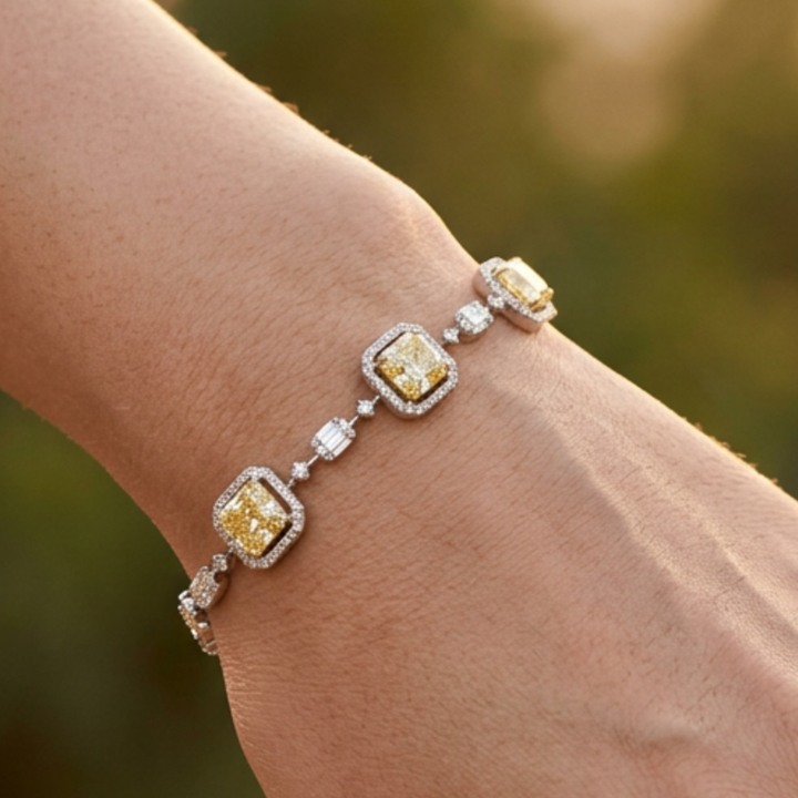 A close-up of a silver-toned bracelet with three yellow gemstones and small clear accent stones, worn on a person's wrist against a softly blurred warm-toned background.