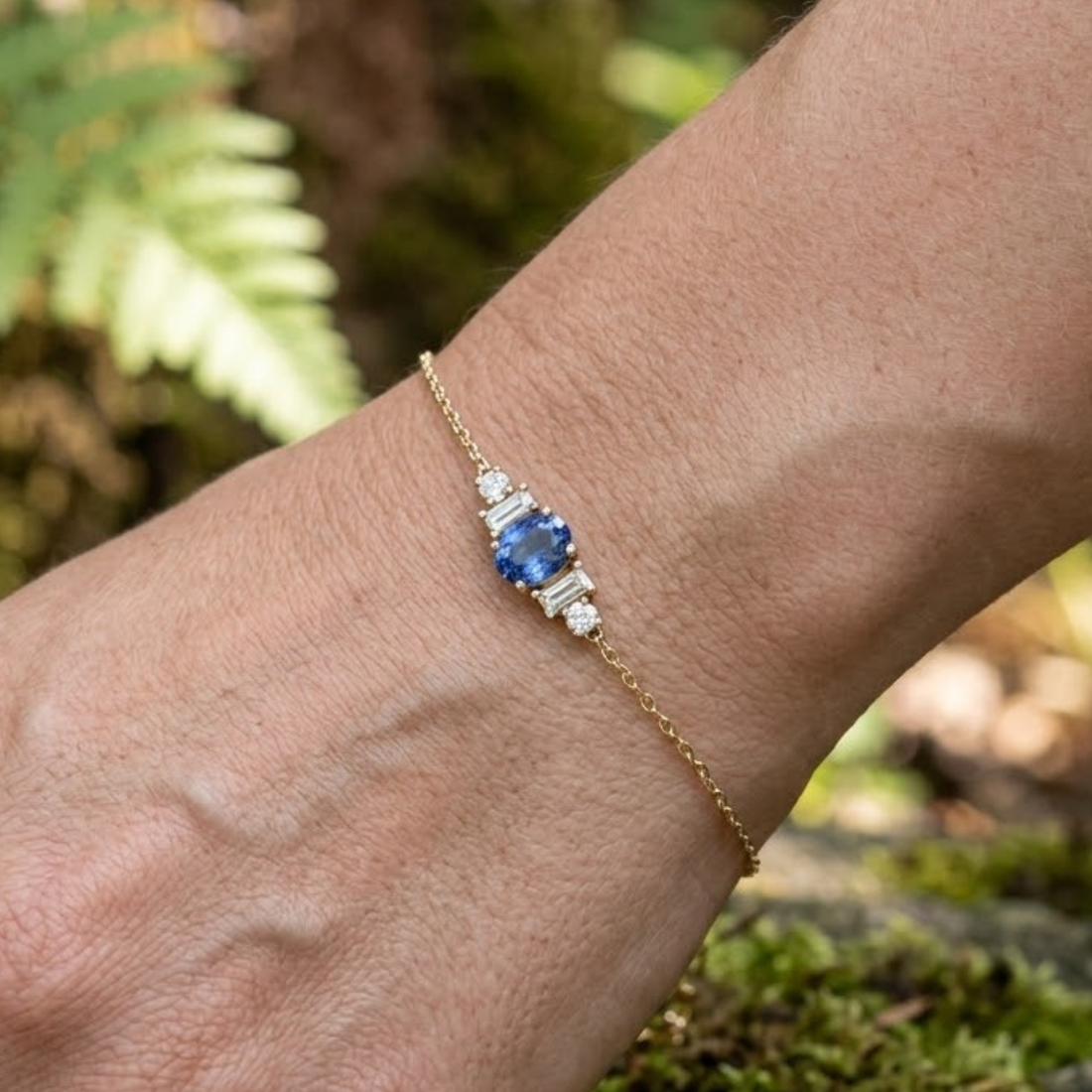 Oval blue gemstone and diamond station bracelet worn on the wrist in yellow gold.