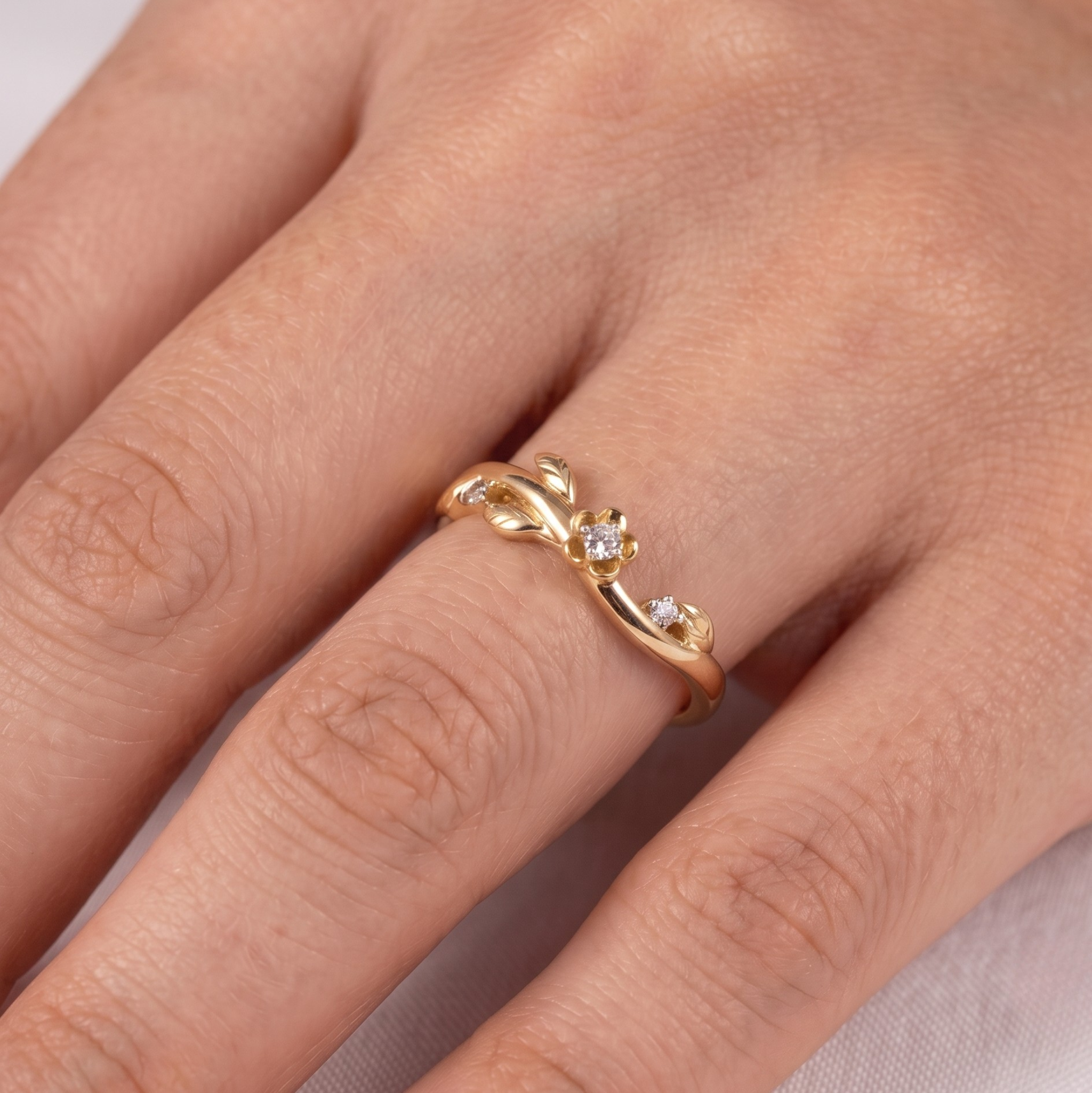 A close-up of a hand wearing a delicate gold ring with small clear gemstones set along a curved, vine-like design.
