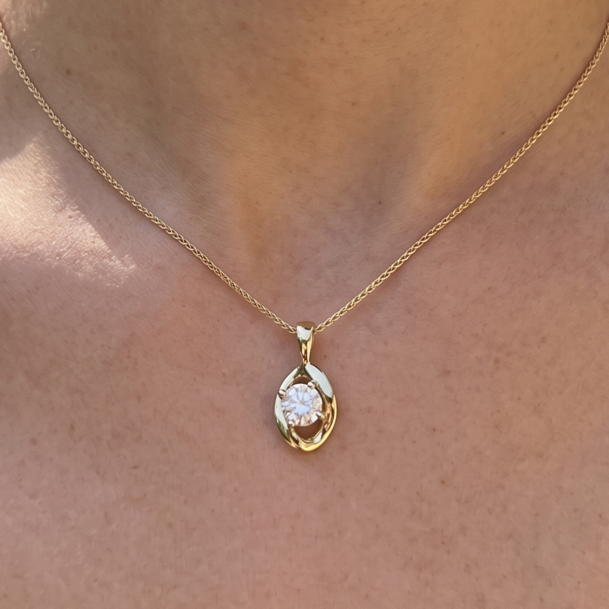 A close-up of a gold chain necklace with a teardrop-shaped pendant featuring a clear round gemstone, worn on a person's neck.