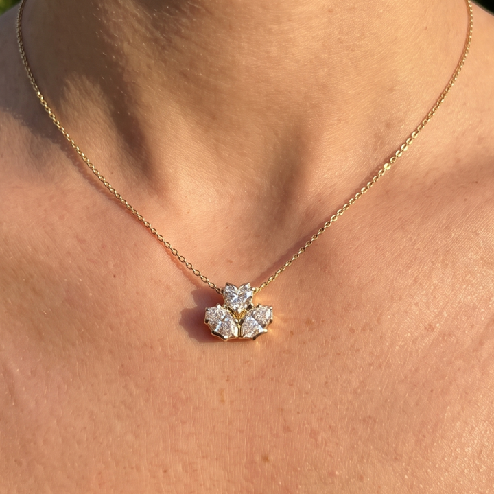 A close-up of a person's neck and chest wearing a delicate gold chain necklace with a small flower-like pendant set with clear stones.