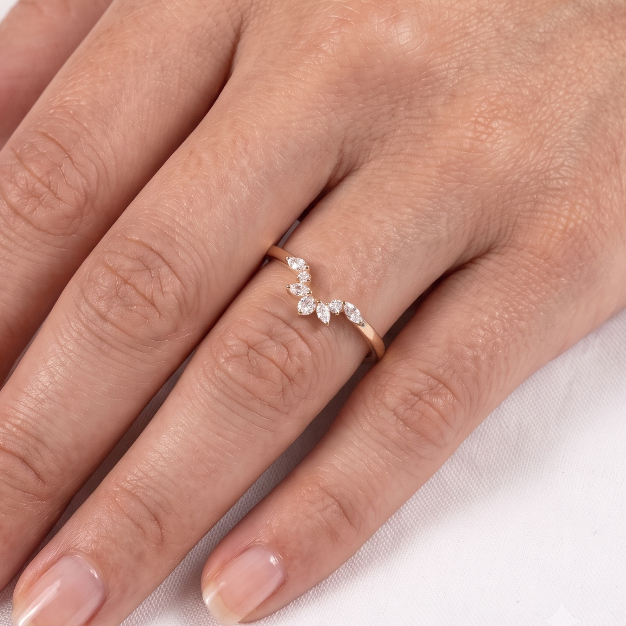 A close-up of a hand wearing a delicate rose gold ring with a small curved row of clear marquise-cut gemstones.