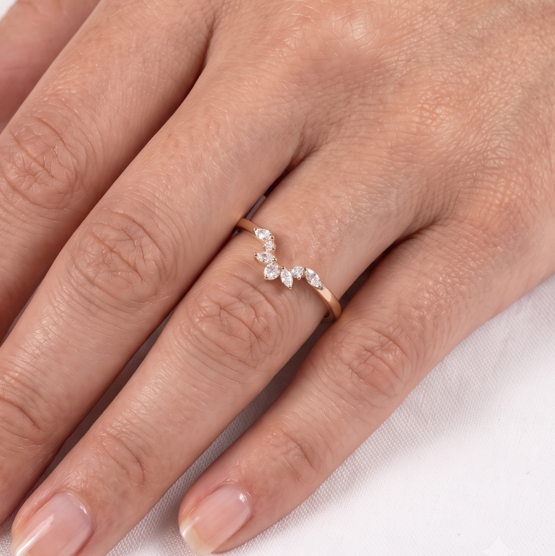 A close-up of a hand wearing a delicate rose gold ring with a small curved row of clear marquise-cut gemstones.