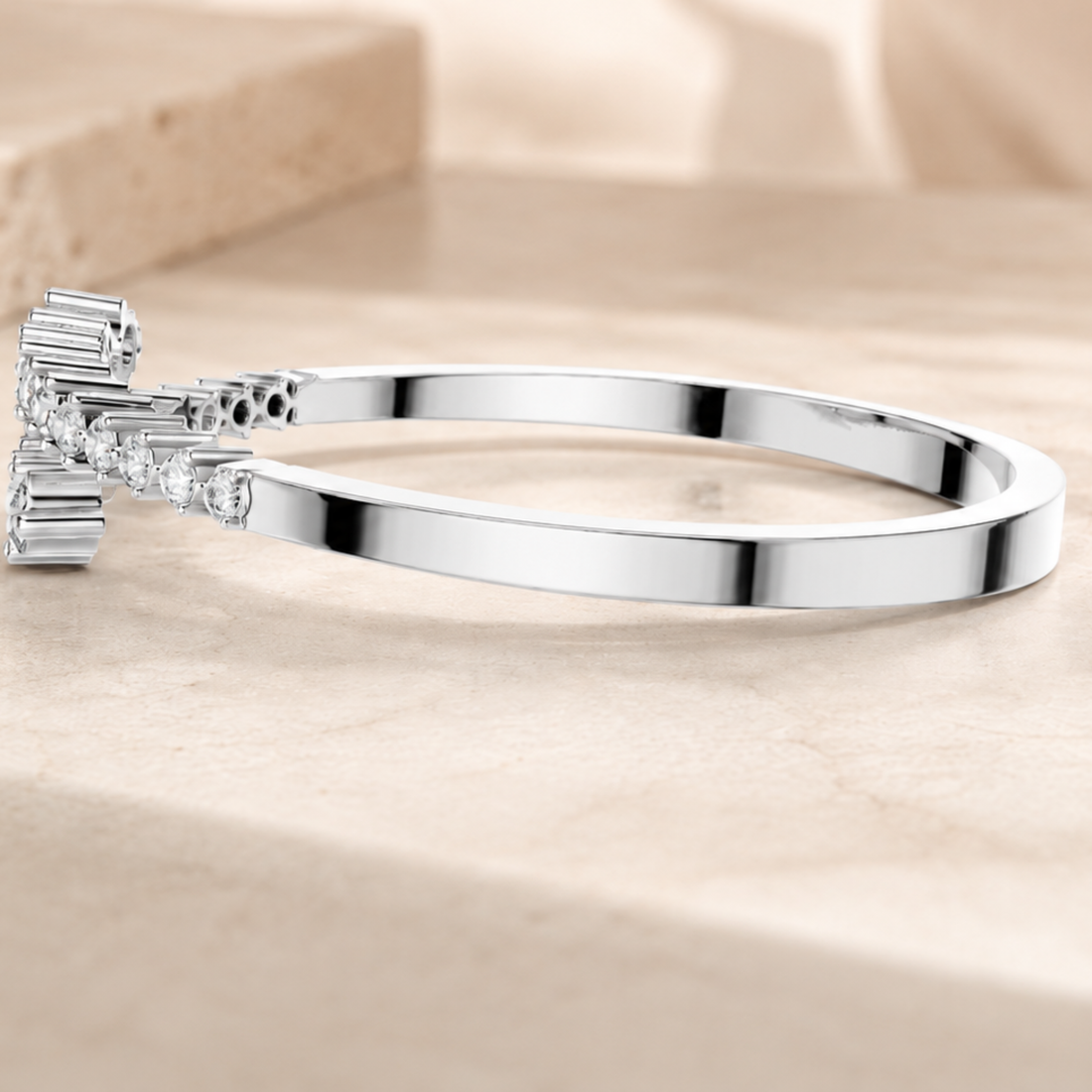 A polished silver-toned bangle bracelet with a decorative rectangular crystal cluster on one end, resting on a light beige stone surface.