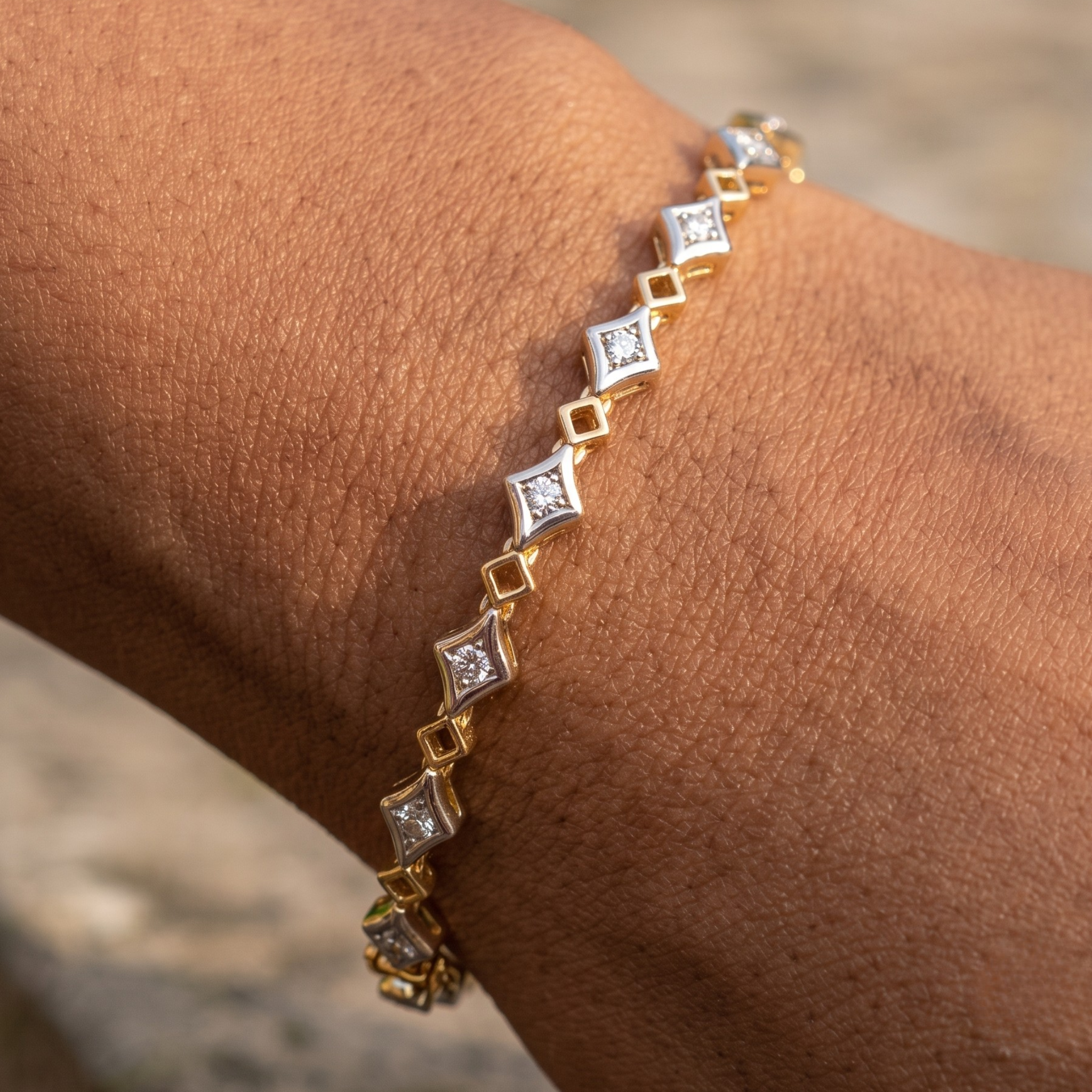 A close-up of a gold bracelet with alternating gold and silver diamond-shaped links, each set with a clear gemstone, worn on a person's wrist.