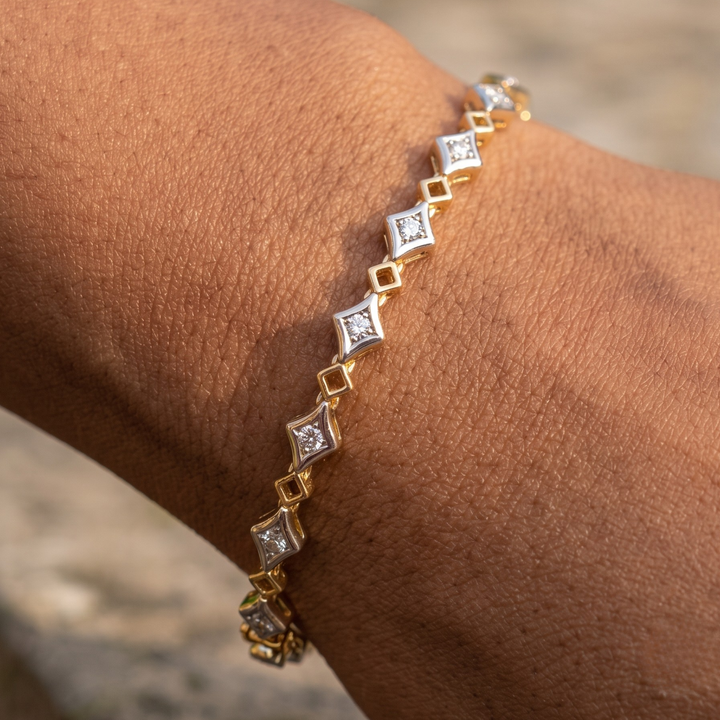 A close-up of a gold bracelet with alternating gold and silver diamond-shaped links, each set with a clear gemstone, worn on a person's wrist.