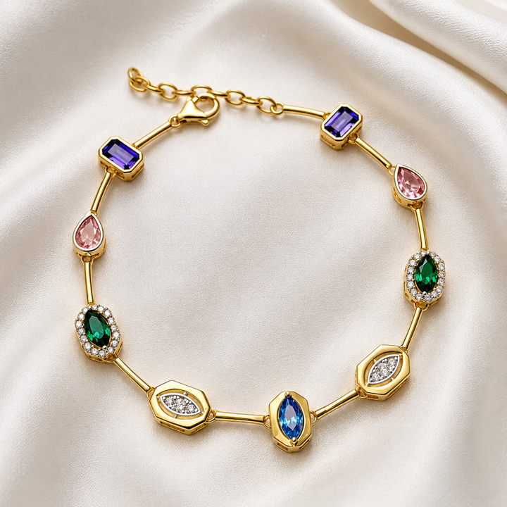 A gold link bracelet featuring multiple colorful gemstones in different shapes, including purple, pink, green, and blue stones, displayed on a draped white satin fabric.