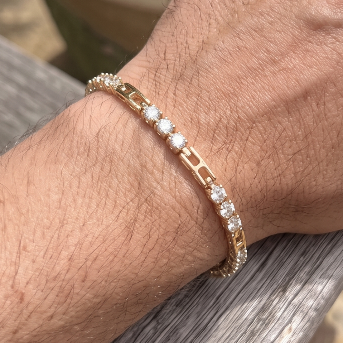 A close-up of a person's wrist wearing a gold tennis bracelet with clear round-cut gemstones, resting on a weathered gray wooden surface.