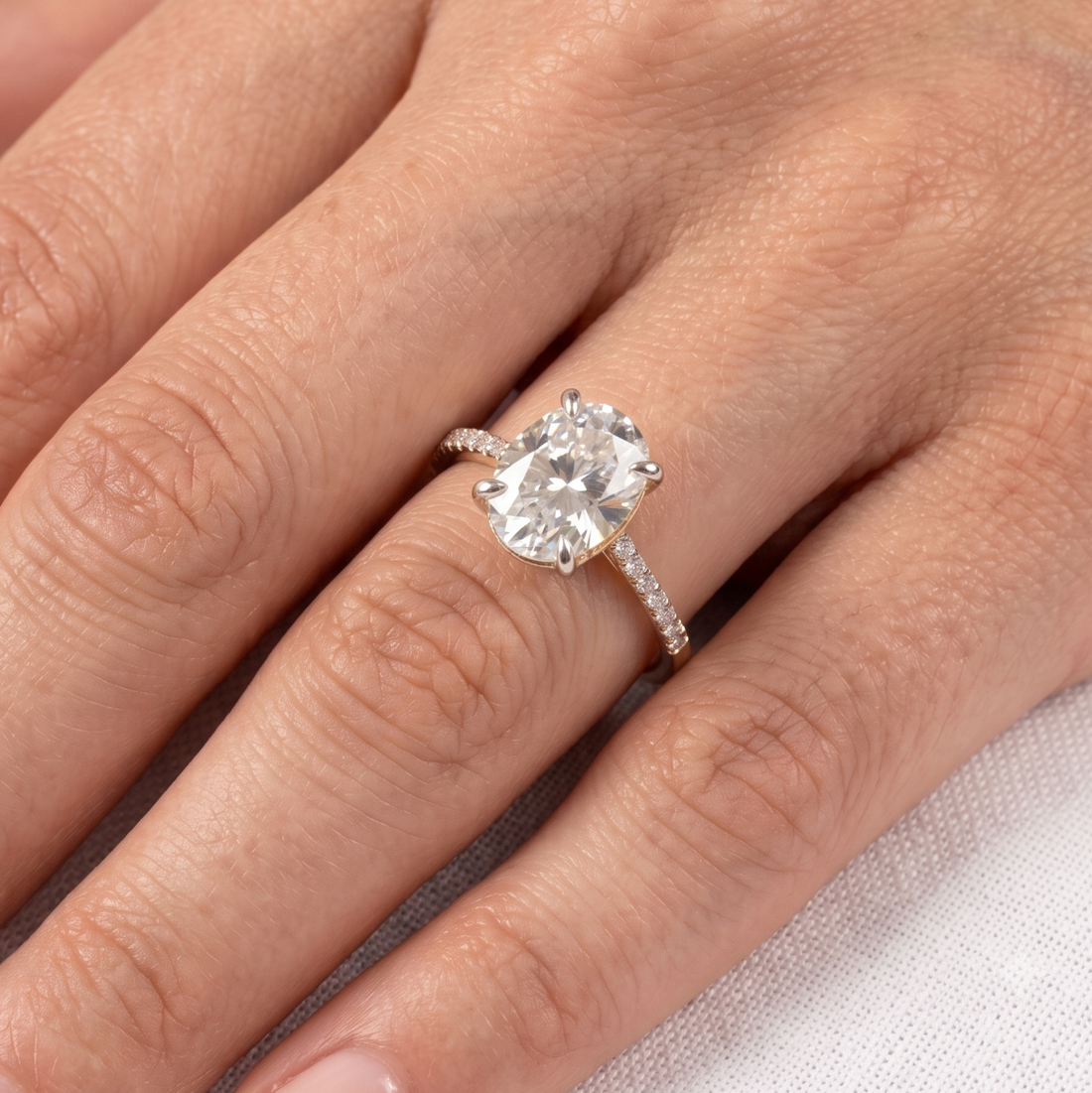 A close-up of a hand wearing a silver-tone ring with a large pear-cut clear gemstone and a pavé band.