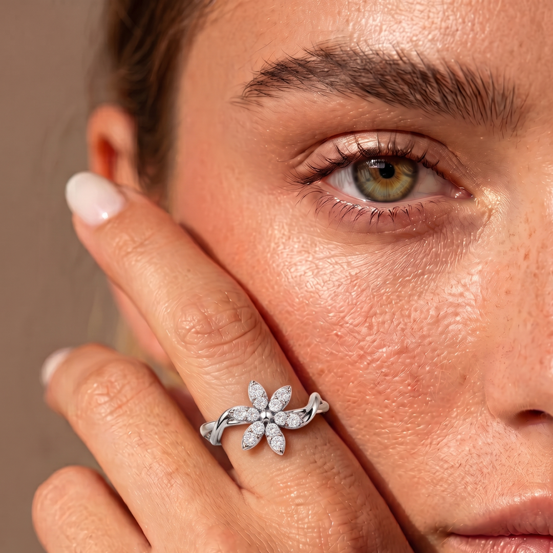 A close-up lifestyle shot of a woman's face and hand, showcasing a silver ring with a flower-shaped pavé setting on her finger.